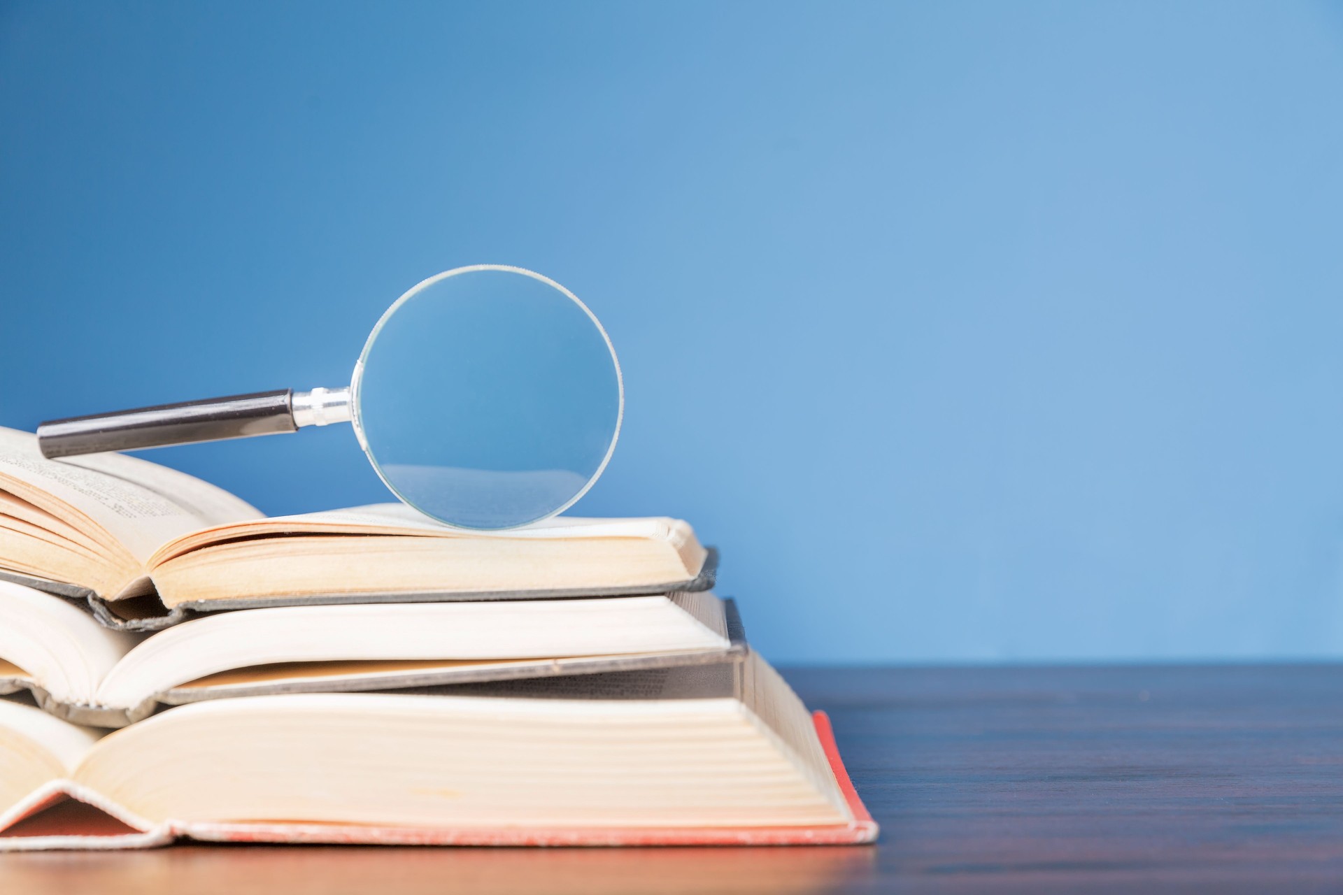 open book with magnifying glass on wooden desk in information library of school or university, concept for education,reading , study, copy space and blue background.